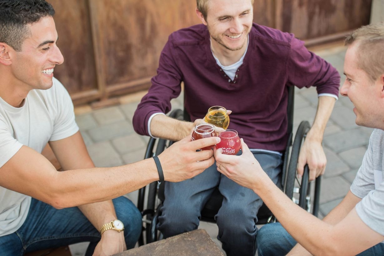 Young man in his wheelchair enjoying drinks with his friends