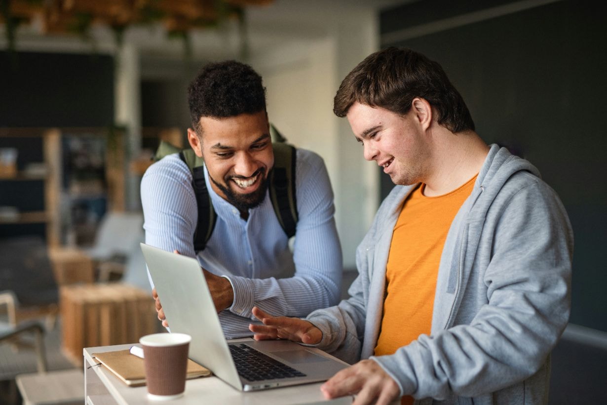 Caregiver helping young boy with Downs syndrome about using computers