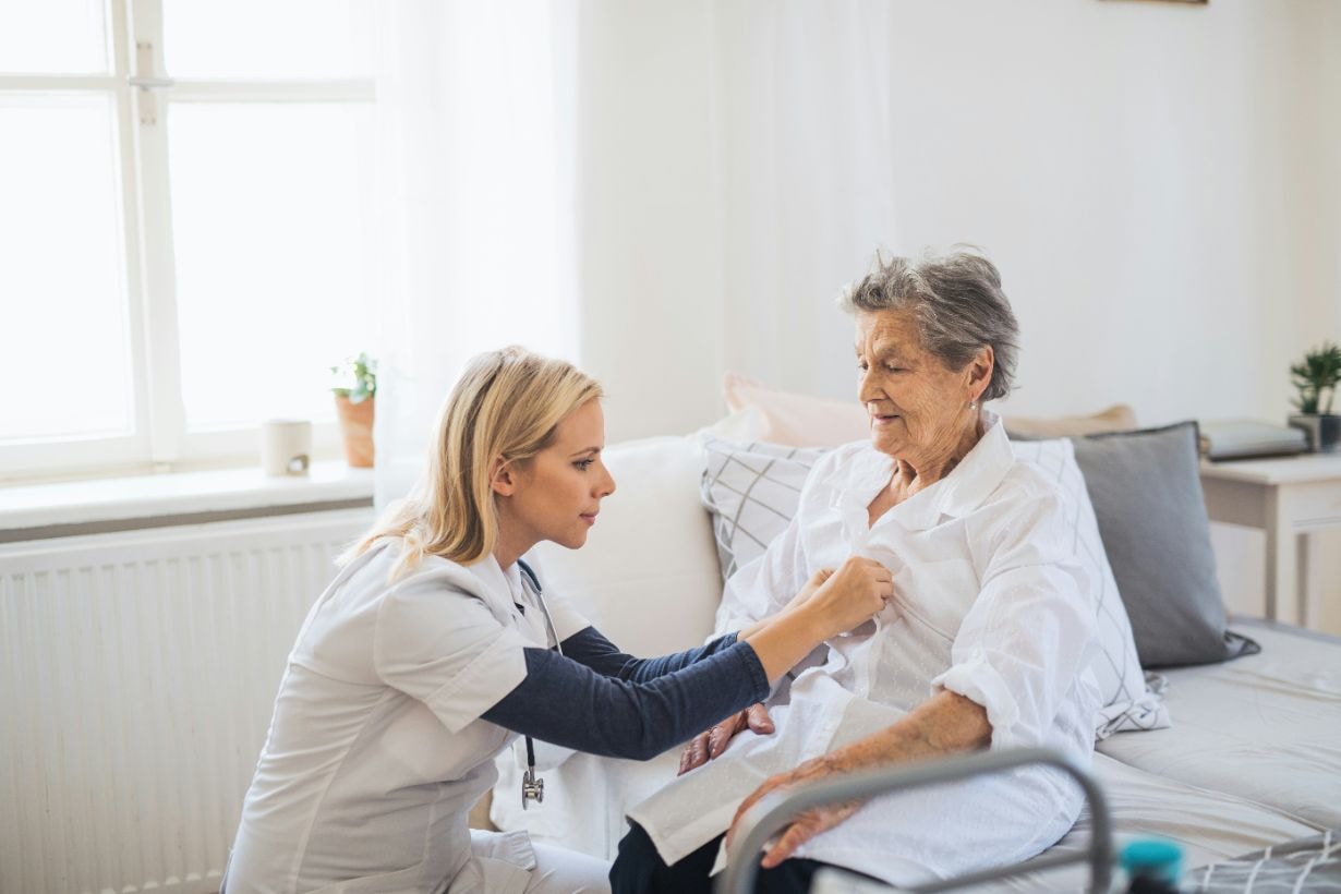 Caregiver helping old woman to dress up